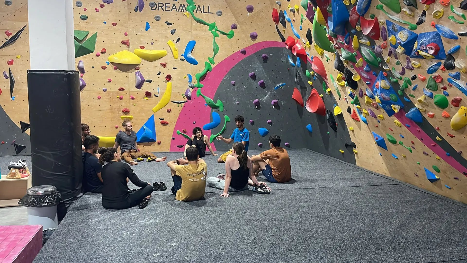 קבוצת מטפסים יושבת יחד על המזרן מול קיר הבולדר של Allé